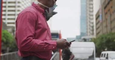 Afrika kökenli Amerikalı bir adam gün boyunca şehir sokaklarında hava kirliliğine karşı maske takıyor ve caddeyi geçerken akıllı telefonunu kullanıyor..
