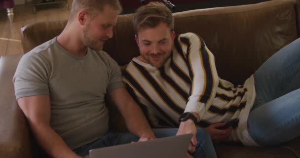 幸せな白人男性の高角度ビュー同性カップルは自宅でリラックスしたリビングルームで ソファに座って話し 一緒にラップトップコンピュータを使用して 社会的距離と隔離された封鎖の自己分離スローモーションで — ストック動画