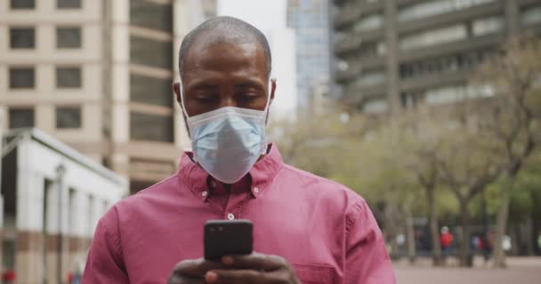 アフリカ系アメリカ人の男性は 大気汚染やCovid19コロナウイルスに対して顔マスクを着用し 彼のスマートフォンを使用して 日中街中で約 — ストック動画