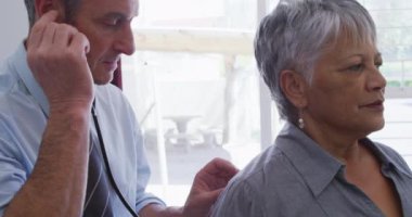 Kafkasyalı erkek doktor, Coronavirus covid19 salgını sırasında üst düzey melez bir kadın hastayı muayene ediyor..