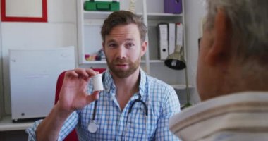 Kafkas erkek doktor kareli gömlek giyiyor, bir huzurevinde ameliyatta çalışıyor, Coronavirus covid19 salgını sırasında beyaz erkek hastaya tedavi yöntemlerini anlatıyor..