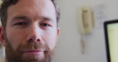 Mavi tişört ve steteskop giyen beyaz bir erkek doktorun portresi. Bir huzurevinde ameliyatta çalışıyor. Gülümsüyor ve doğrudan kameraya bakıyor..