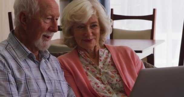 上了年纪的白种人夫妇一起呆在家里 坐在沙发上 用手提电脑与家人交流 共同应对考拉病毒大流行 — 图库视频影像