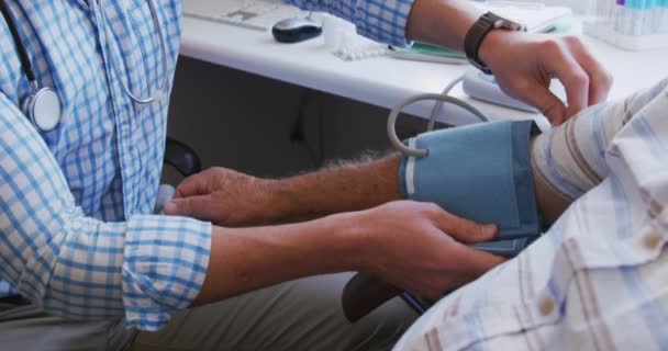 白种人医生身穿格子衬衫 在一家养老院做手术 测量一位老年白种人男性病人在大流行病中的血压 — 图库视频影像