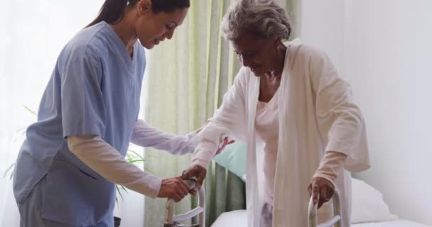 Кавказская Медсестра Синем Халате Помогающая Пожилой Афроамериканке Ходить Ходячей Рамой — стоковое видео