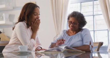Kıdemli melez kadın evde eğleniyor, kızıyla vakit geçiriyor, çay içiyor, birlikte dergi okuyor, sosyal uzaklık ve kendini tecrit altında tutuyor, yavaş çekimde.