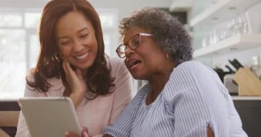 Kıdemli melez kadın evinde eğleniyor, kızıyla vakit geçiriyor, çay içiyor, birlikte dijital tablet kullanıyor, sosyal uzaklık ve kendini tecrit altında tutuyor, yavaş çekimde.