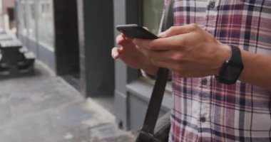 Kafkasyalı bir adamın gündüz vakti şehir sokaklarında dolaşması, akıllı saat takması ve akıllı telefon kullanması..