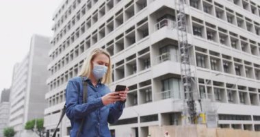 Beyaz kadın, Coronavirus 'a karşı yüz maskesi takıyor. Gün boyunca şehir sokaklarında dolaşırken, akıllı telefonunu kullanıyor..