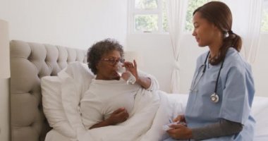 Melez bir ırk hemşiresi tarafından evinde ziyaret edilen melez bir kadın içme suyu, sosyal mesafeler ve yavaş çekimde karantinaya alınan kendini izole etme.