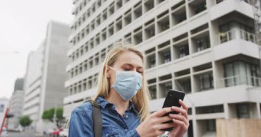 Beyaz kadın, Coronavirus 'a karşı yüz maskesi takıyor. Gün boyunca şehir sokaklarında dolaşırken, akıllı telefonunu kullanıyor..