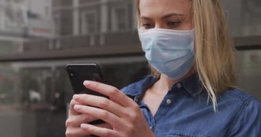 Beyaz kadın, Coronavirus 'a karşı yüz maskesi takıyor. Gün boyunca şehir sokaklarında dolaşırken, akıllı telefonunu kullanıyor..