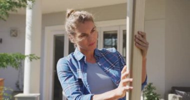 Beyaz bir kadının portresi, bahçesinde vakit geçirip evini yeniliyor, sosyal uzaklık ve karantinaya alınıyor, Coronavirus covid 19 salgını sırasında karantina altına alınıyor, elinde ahşap bir tahtayla kameraya bakıyor ve yavaş çekimde gülümsüyor.