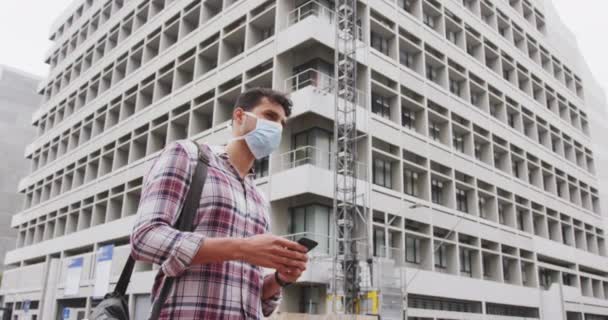 一个白种人头戴口罩面对考罗纳维的画像 白天在城市街道上边走边用他的智能手机 — 图库视频影像