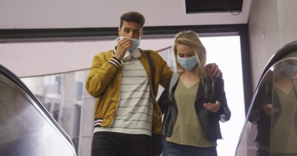 コロナウイルス対策顔マスクを身に着けている白人カップル Covid 19地下鉄駅のエスカレーターに立って 彼らのスマートフォンを使用して — ストック動画