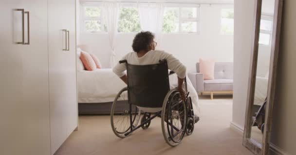 年长的男女混血女子享受着在家里的时光 坐在轮椅上 与外界保持距离 在隔离中自我隔离 动作缓慢 — 图库视频影像