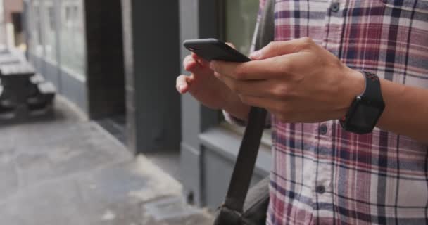 一个白人男子的中段在城市街道上走来走去 他穿着一件时髦的衣服 用的是智能手机 — 图库视频影像