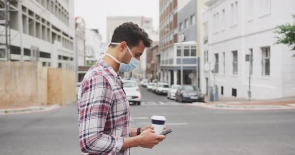 女性が通りを通っている間 彼のスマートフォンを使用して 昼間の街の通りに19をCovid コロナウイルスに対する顔マスクを身に着けている白人男性の肖像画 — ストック動画