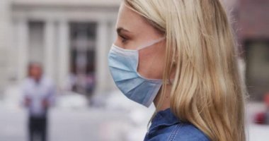 Beyaz kadın, Coronavirus 'a karşı maske takıyor. Gün boyunca şehir sokaklarında dolanıp kameraya bakıyor..
