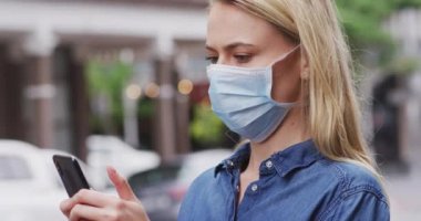 Beyaz kadın, Coronavirus 'a karşı yüz maskesi takıyor. Gün boyunca şehir sokaklarında dolaşırken, akıllı telefonunu kullanıyor..