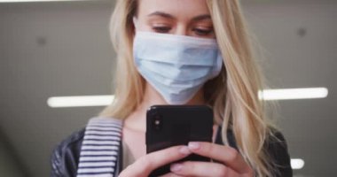 Beyaz kadın, Coronavirus 'a karşı yüz maskesi takıyor. Gün boyunca şehir sokaklarında dolaşırken, akıllı telefonunu kullanıyor..