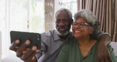 Afrika kökenli yaşlı bir çift, Coronavirus covid 19 salgını sırasında karantinada birlikte vakit geçiriyorlar. Akıllı telefon tutan ve yavaş çekimde selfie çeken bir adam.