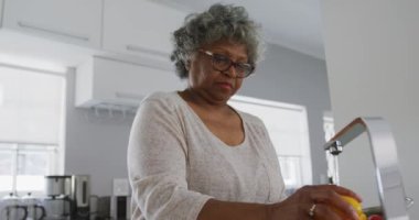 Kıdemli bir Afrikalı Amerikalı kadın, Coronavirus covid 19 salgını sırasında karantinada karantina ve kişisel izolasyon ile evde vakit geçiriyor. Yavaş çekimde biber yıkıyor.