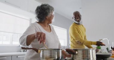 Üst düzey bir Afrikalı Amerikalı çift, Coronavirus covid 19 salgını sırasında karantinada karantina ve kendilerini izole etmek için evde vakit geçiriyorlar. Mutfakta durup ağır çekimde yemek hazırlıyorlar.