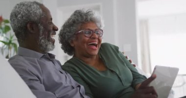 Kıdemli bir Afrikalı Amerikalı çift, Coronavirus covid 19 salgını sırasında karantinada karantinada birlikte vakit geçiriyorlar. Tablet kullanıyorlar, arkadaşlarına ya da akrabalarına video araması yapıyorlar, yavaş çekimde el sallıyorlar.