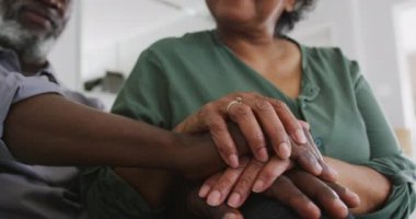 Afrika kökenli yaşlı bir çift, Coronavirus covid 19 salgını sırasında karantinada birlikte vakit geçiriyorlar. Kanepede oturup el ele tutuşuyorlar ve ağır çekimde gülümsüyorlar.