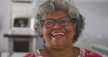 Yaşlı bir Afrikalı Amerikalı kadının portresi, karantinada karantina altında geçirdiği zaman, sosyal uzaklık ve kendini izole etme Coronavirus covid 19 salgını sırasında kameraya bakıyor ve yavaş çekimde gülümsüyor.