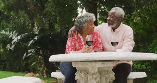 一对资深的非洲裔美国夫妇一起在自家的花园里度过时光 他们在科罗纳维病流行期间 彼此疏远 自我隔离 坐在桌旁聊天 桌上拿着酒杯喝红酒 — 图库视频影像