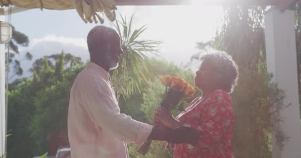 一对资深的非洲裔美国夫妇在他们的花园一起度过了一段时光 他们在科罗纳维病流行期间 在隔离过程中保持距离和自我隔离 男人捧着一束鲜花 微笑着把它们送给了女人 — 图库视频影像