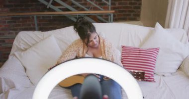 Beyaz kadın vlogger evde, oturma odasında, online blogu için gitar çalmayı öğretiyor. Karantina karantinasında sosyal uzaklık ve kişisel izolasyon.