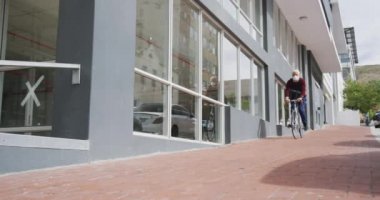 Orta yaşlı, beyaz bir adam gün boyunca şehir sokaklarında dolaşır, Coronavirus 'a karşı maske takar, covid 19, yavaş çekimde bisiklet sürer..