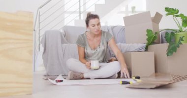 Beyaz bir kadın, Coronavirus covid 19 salgını sırasında karantinada evini, sosyal mesafeyi ve kendini izole ederek evde vakit geçiriyor. Bir yerde oturuyor, mimari planlar okuyor, kupa tutuyor, yanında da bir köpek oturuyor.