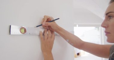 Beyaz bir kadının evde vakit geçirmesini, evini yenilemesini, sosyal mesafeyi ve Coronavirus covid 19 salgını sırasında karantinaya alınmasını, ruh seviyesini, duvar uzunluğunu ölçümlemesini ve işaretlemesini kapatın. 