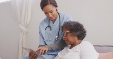 Karışık ırktan bir kadın, dijital tablet, sosyal uzaklık ve kendini izolasyon kullanarak yavaş çekimde karantinaya alınan melez bir hemşire tarafından evinde ziyaret ediliyor.