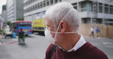 Orta yaşlı, beyaz bir adam gün boyunca şehir sokaklarında dolaşır, Coronavirus 'a karşı yüz maskesi takar, covid 19, yavaş çekimde şehri keşfeder..