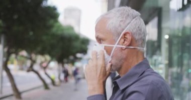 Orta yaşlı beyaz bir adam gün boyunca şehir sokaklarında dolaşır, Coronavirus 'a karşı yüz maskesi takar, covid 19, ağır çekimde.