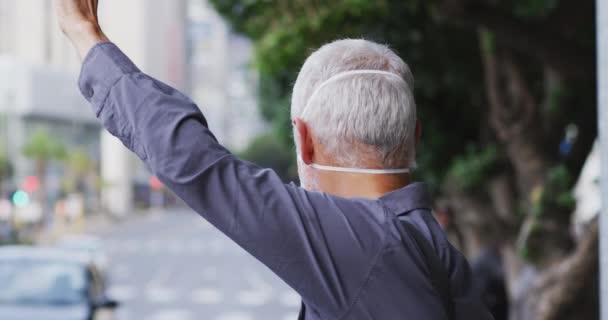 白种人中年男子白天在城市街道上走来走去 头戴口罩 头戴眼镜片 慢吞吞地招呼出租车 — 图库视频影像