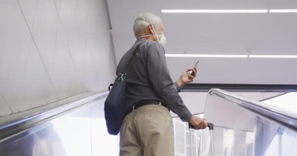 中年男子头戴口罩 头戴眼镜片 头戴眼镜片 在地铁站用自动扶梯 提着手提箱 用智能手机 动作缓慢 — 图库视频影像