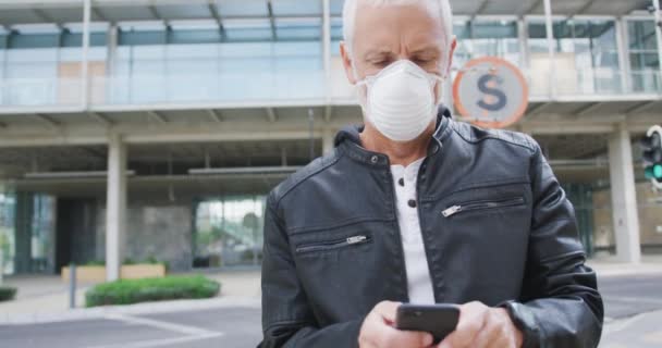 一日中街中で白人の中年男性が顔のマスクをつけてコロナウイルスに対抗し19歳でスマートフォンを使いスローモーションで — ストック動画