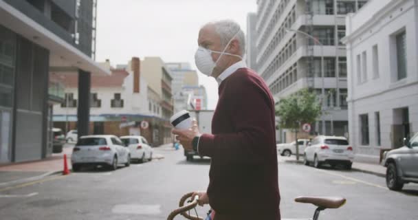 コロナウイルスに対してフェイスマスクを着用し 19をCovid 彼の自転車を回転させ ゆっくりと動きながらテイクアウトコーヒーを保持 — ストック動画