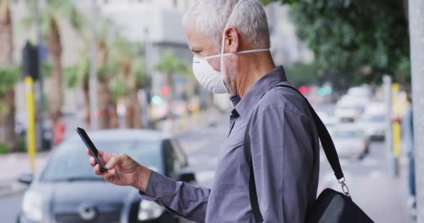 白种人中年男子白天在城市街道上走来走去 头戴口罩 头戴眼镜片 用智能手机 动作缓慢 — 图库视频影像