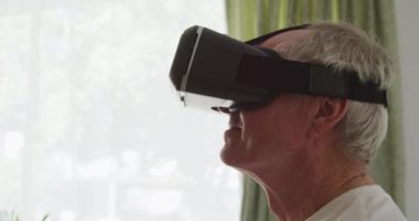 Kafkasyalı bir adamın sanal gerçeklik kulaklığı takıp, etrafa bakıp gülümseyen, Coronavirus covid19 salgını sırasında bir huzurevinde izole ve sosyal mesafeli bir görünüm. Ağır çekimde