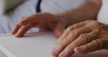 Tekerlekli sandalyede oturan, gözleri kapalı, kör alfabesiyle kitap okuyan, Coronavirus Covid19 salgını sırasında huzurevinde sosyal mesafeyi izole eden, yaşlı beyaz bir adam. Ağır çekimde