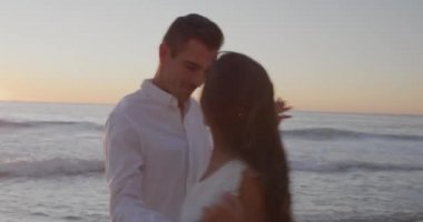 Gün batımında sahilde dans eden genç ve mutlu beyaz bir çiftin yan görüntüsü. Sahilde yaz aşkı.