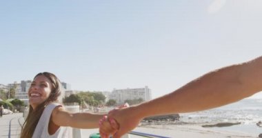 Deniz kenarında genç ve mutlu bir beyaz kadının ön planda eşiyle el ele yürüdüğünü, kolunu çekip gülümsediğini ve ağır çekimde gülümsediğini gördüm.