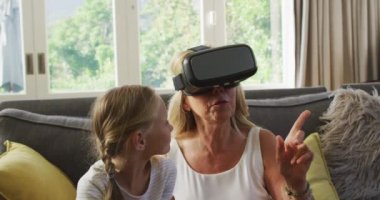 Kafkasyalı bir kız, büyükannesiyle birlikte kanepede oturmaktan keyif alıyor. Bir kadın, koronavirüs salgını sırasında karantinaya alınırken, ağır çekimde, VR kulaklık takıyor, sosyal uzaklık ve kendini izole ediyor.
